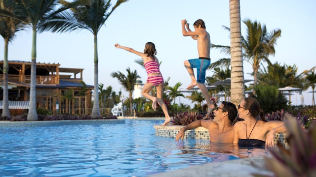 Två föräldrar sitter vid poolkanten medans två barn hoppar i vattnet. Låt inte flygpriser bestämma resan, dra nytta av NCLs flygrabatt.