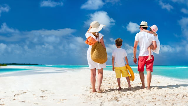 Bilden visar en familj som går på en vacker strand med turkost vatten vid sidan.