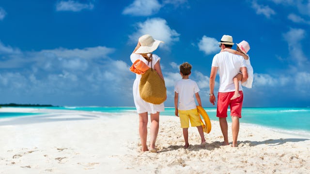 Bilden visar en familj som går på en vacker strand med turkost vatten vid sidan.