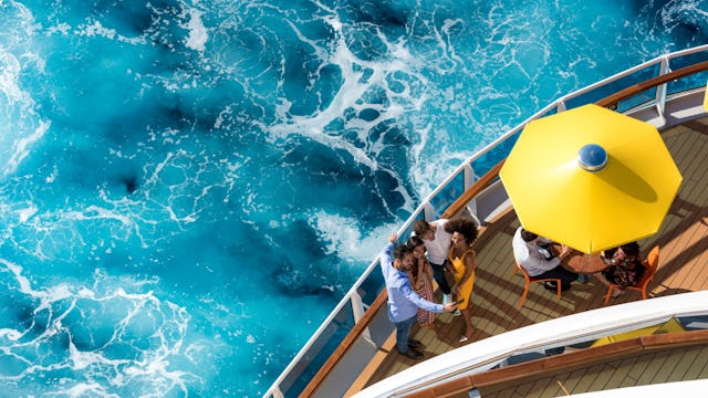 Bilden visar en familj som står på akterdäck. Man ser havet och ett gult parasoll på däck också.