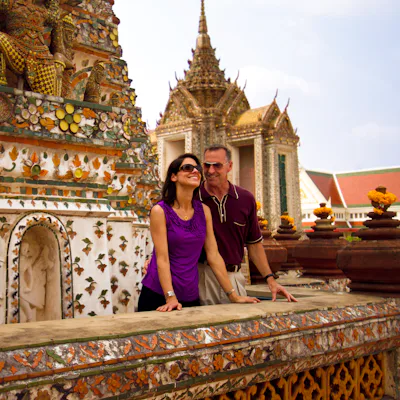 Bilden visar ett par framför en rikt utsmyckad byggnad i Bangkok