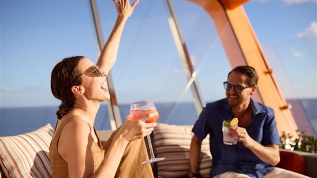 Bilden visar två personer som sitter och tar en drink på Celebrity Apex Magic Carpet.