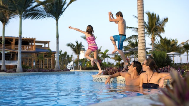Två föräldrar sitter vid poolkanten medan två barn hoppar i vattnet. Låt inte flygpriser bestämma resan, dra nytta av Norwegian Cruise Lines flygrabatt.