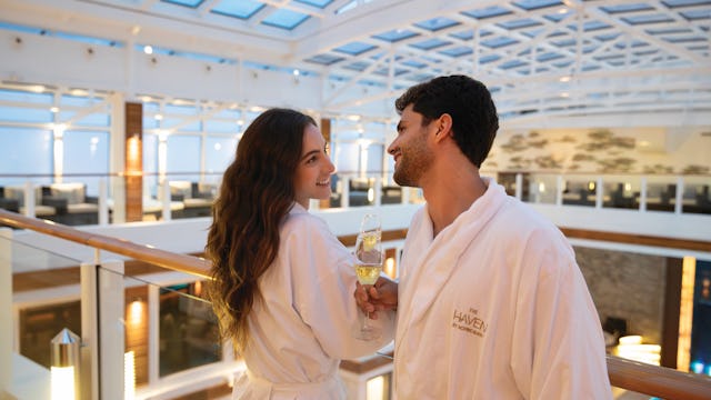 Lyxkryssning med Norwegian Cruise Line. Upplev the Haven ombord. Bilden visar två personer i the Haven ombord ett Norwegian Cruise Line fartyg som skålar med ett glas bubbel.