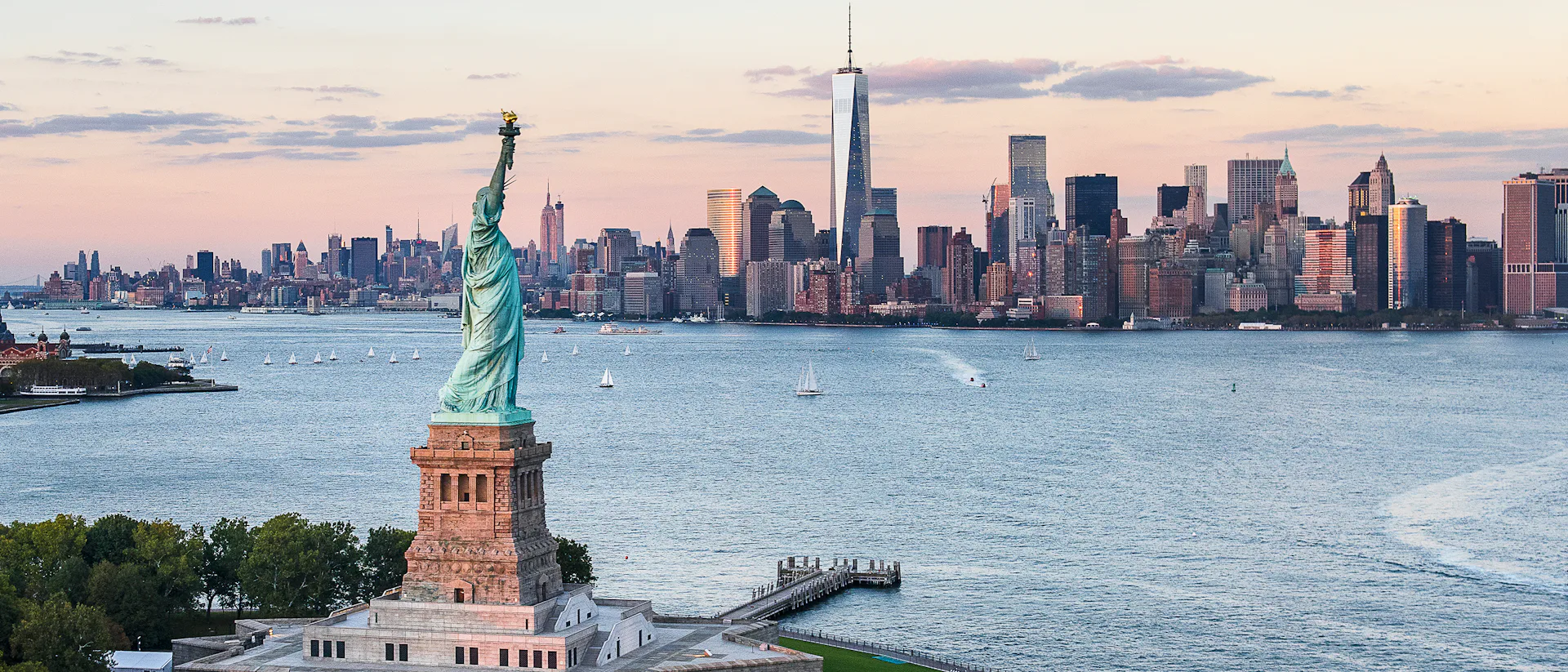 Kryssa till USA eller utgå från USA på din kryssning. Bilden visar en översikt över New York från vattnet med Frihetsgudinnan i förgrunden