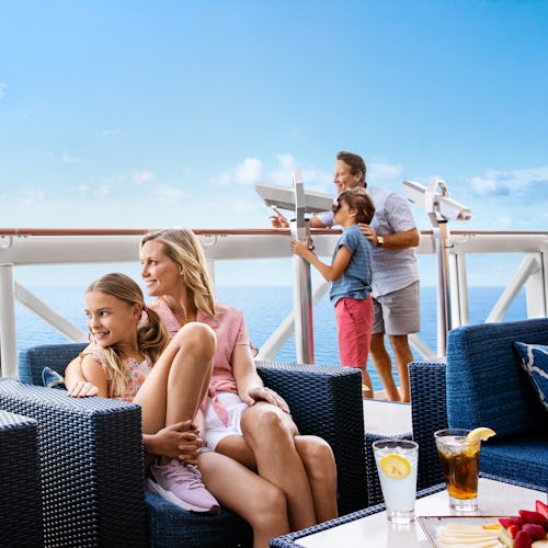 Bilden visar en familj där två sitter i soffan och två står vid fartygets räcke och kollar i en kikare. Upptäck våra tips om att kryssa med barn.