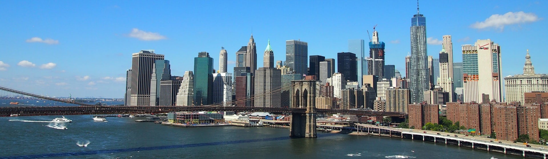 Kryssa till eller från New York. Bilden visar Brooklyn Bridge och New Yorks stads silhuett från vattnet.