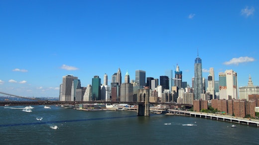 Kryssa till eller från New York. Bilden visar Brooklyn Bridge och New Yorks stads silhuett från vattnet.