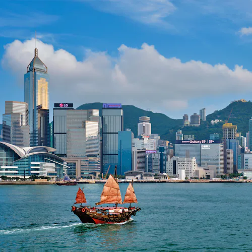 Kryssa jorden runt och upplev det bästa från Asien och resten av världen. Bilden visar stadssilhuetten av Hong Kong från vattnet med en båt i förgrunden.