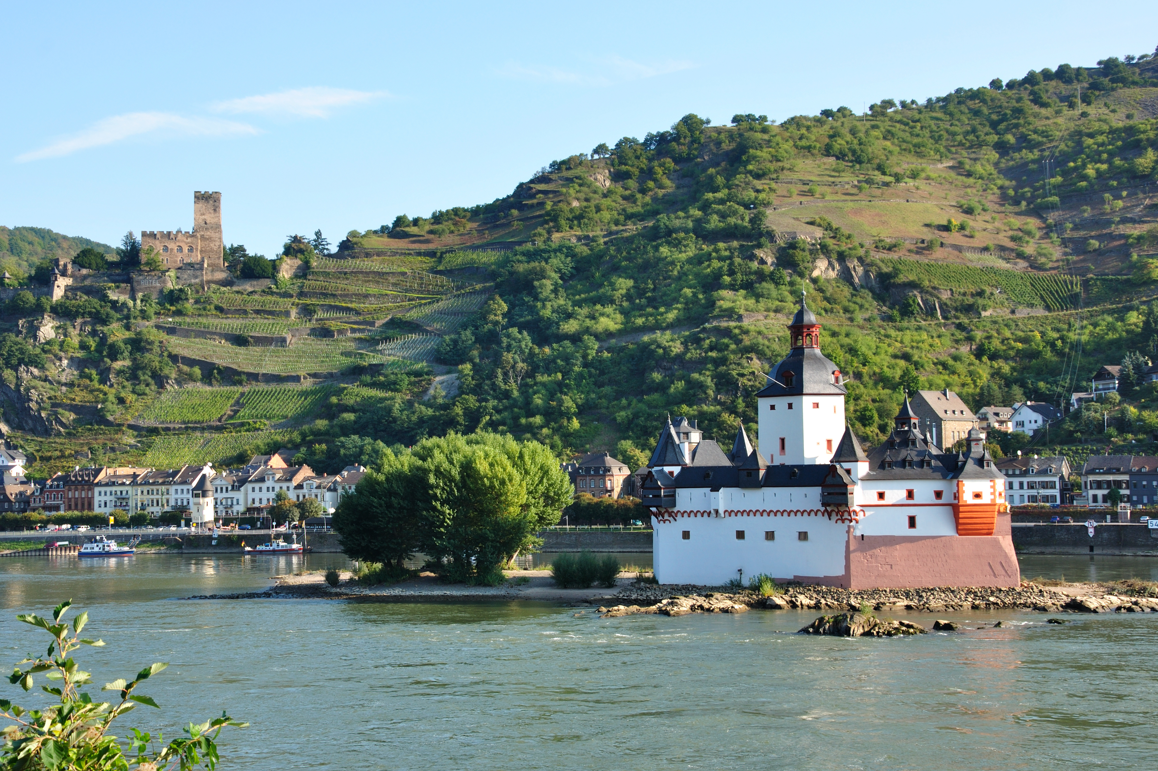 Bilden visar en vacker grönskande vinstad i Tysklandm, Bacharach, med floden Rhen i förgrunden. 