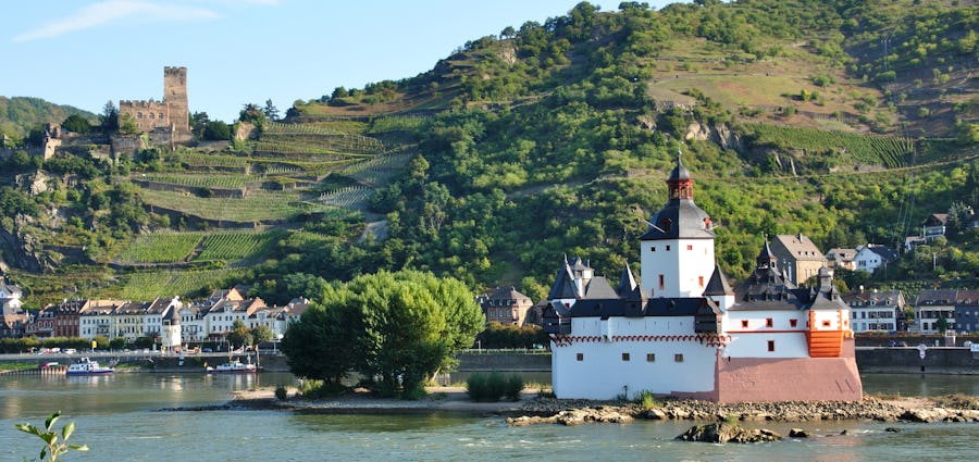 Bilden visar en vacker grönskande vinstad i Tysklandm, Bacharach, med floden Rhen i förgrunden.