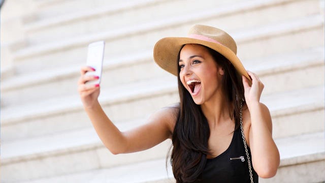 Bilden visar en glad ung kvinna i solhatt som tar en selfie.