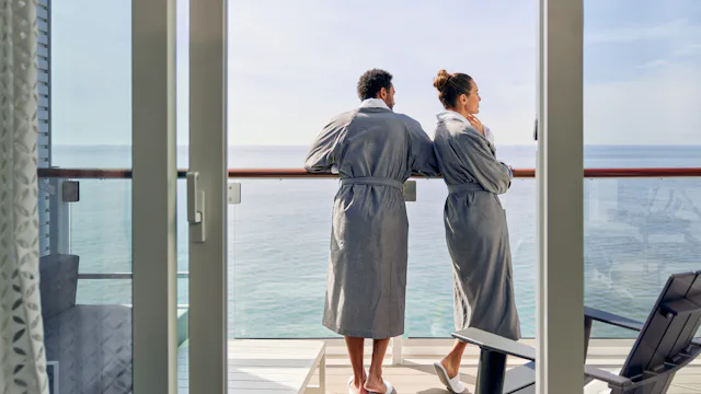 Bilden visar en man och en kvinna i morgonrockar som står på sin balkong i hytten och tittar ut över vattnet.