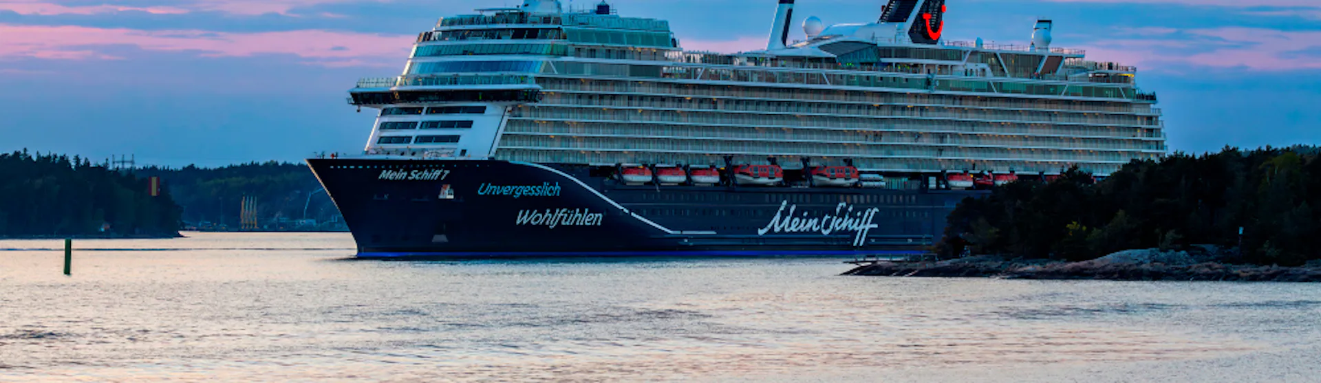 Bilden visar Mein Schiff 7 i hamn i en fantastisk solnedgång.